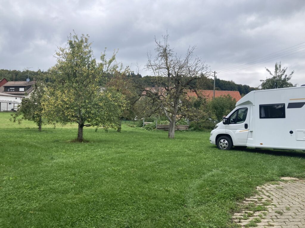 Wohnmobil steht auf einem Stellplatz mit Wiese und Bäumen